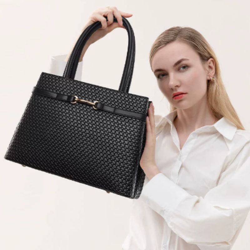 Woman holding a black woven handbag against a plain background